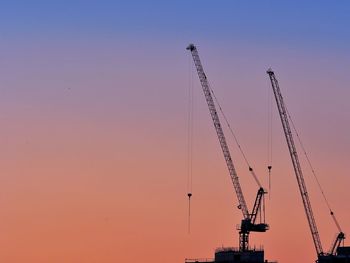 Low angle view of silhouette cranes against sky during sunset