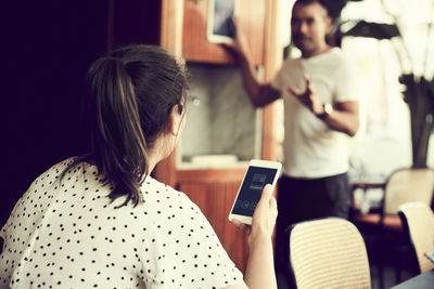 Rear view of female with smart phone talking to male in cafe