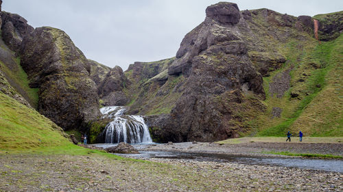 A few people admire waterfall called stjornarfoss between towering cliffs during summer in iceland