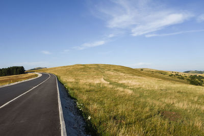 Empty road amidst field against sky