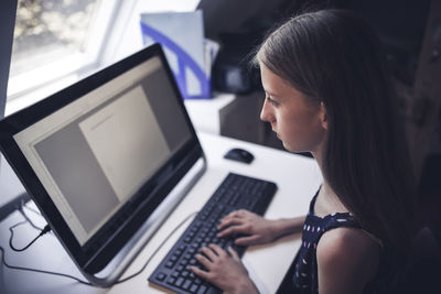 Side view of girl using computer while sitting on table
