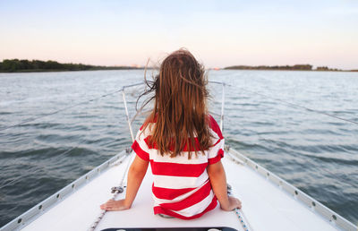 Rear view of girl sitting on boat in sea