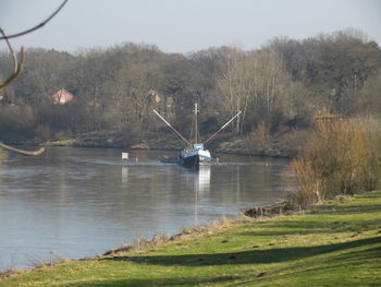 Boat sailing on river by trees against sky