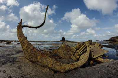 Rusty metallic structure on beach against sky