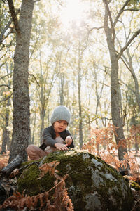 Cute girl playing while sitting on rock in forest