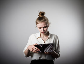 Young woman holding camera while standing against gray background