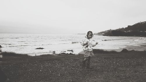 Girl standing on shore at beach against sky