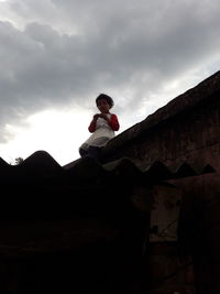 Low angle view of man sitting on mountain against sky