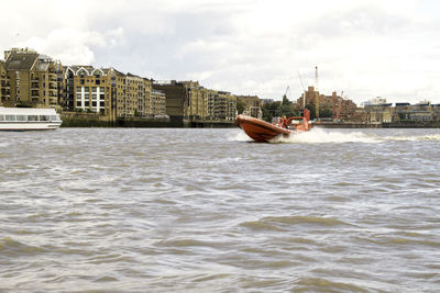 Boat sailing in sea by city against sky