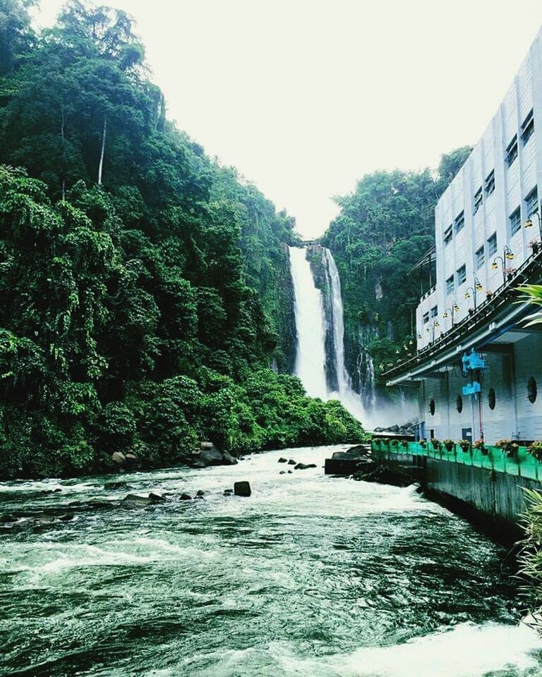 water, tree, waterfall, flowing water, motion, flowing, built structure, architecture, beauty in nature, nature, long exposure, scenics, waterfront, river, clear sky, day, building exterior, fountain, green color, outdoors