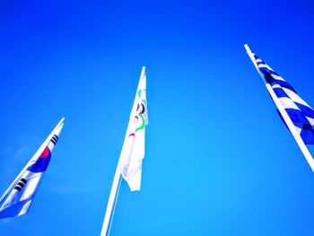 Low angle view of flags against clear blue sky