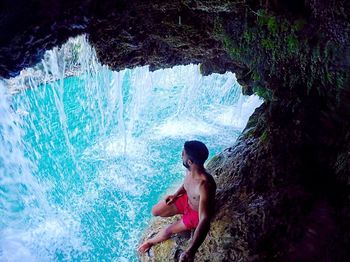 Young man surfing on rock in sea