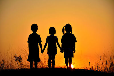 Silhouette children standing on land against orange sky