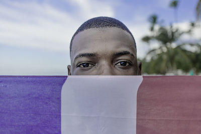 African american male covering face with flag of dominican republic on summer weekend day on beach