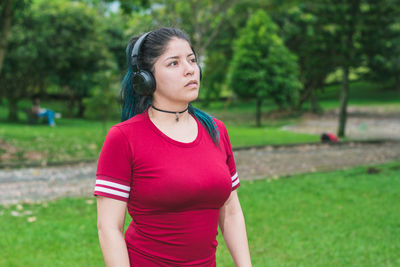 Beautiful college woman with blue hair and red dress listening to music with her wireless headphones