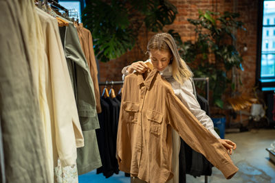 Passionate calm woman try on clothing items on hanger in apparel shop. second hand, department store