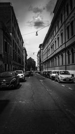 Cars on city street by buildings against sky