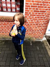 Full length of boy standing against brick wall