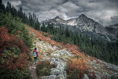 Rear view of woman hiking on mountain against cloudy sky