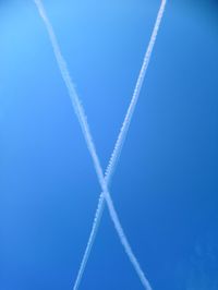 Low angle view of vapor trails against clear blue sky