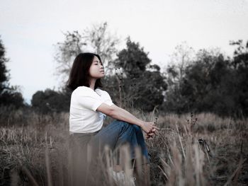 Side view of young woman sitting on field against sky