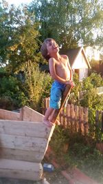 Full length of shirtless boy jumping against trees