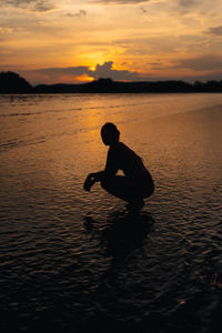 Side view of man jumping in sea during sunset