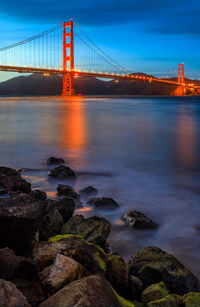 Suspension bridge over sea against sky at night