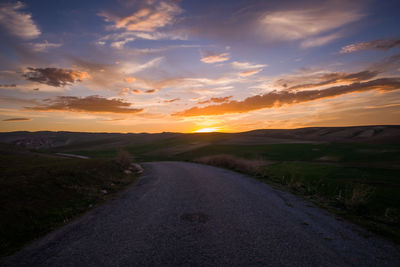 Road amidst field against sky during sunset