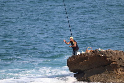 Man fishing on rock by sea