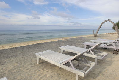 Deck chairs on beach against sky