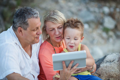 Grandparents with grandson using digital tablet while sitting at beach