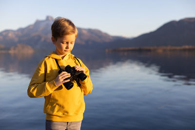 Boy standing against lake holding binocular