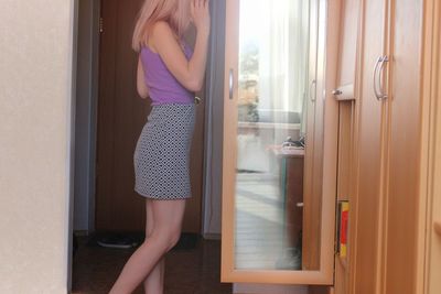 Side view of young woman standing by cabinet at home
