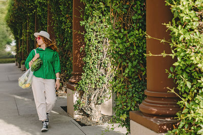 Young woman walking on the street holding a mesh bag with vegetables on her shoulder. 