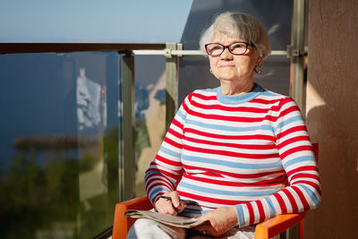 Senior woman in glasses sitting on balcony near the sea