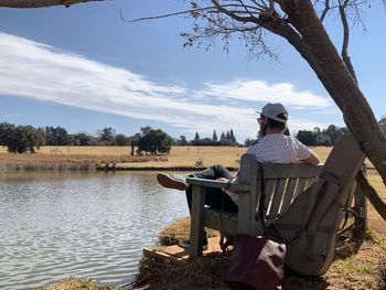 Man sitting by lake against sky