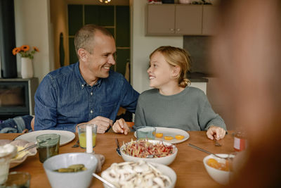 Happy father and son sitting near dining table for lunch at home