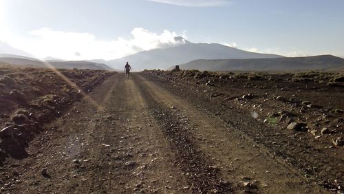 Hiker walking on landscape against sky during sunny day