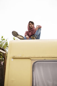 Low view of a young boy sitting on the top of a caravan