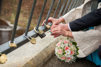 Cropped hands of newlywed couple hanging love lock on bridge