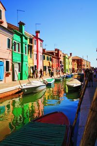 Boats moored in canal by buildings against blue sky