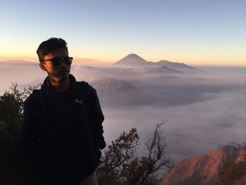 Young man standing by mountains against sky during sunset