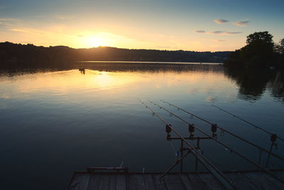 Fishing rods over lake against sky during sunset