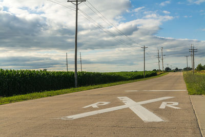 High angle view of railroad crossing sign on road against cloudy sky during sunny day