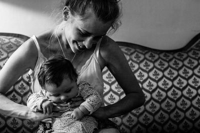 Smiling young woman holding daughter on sofa at home