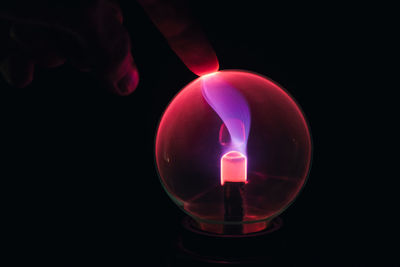 Close-up of hand holding lit candle against black background