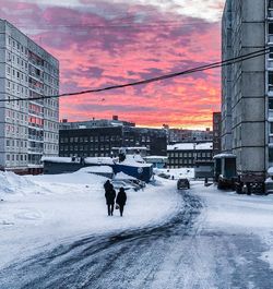 Rear view of people walking on snow covered street against sky