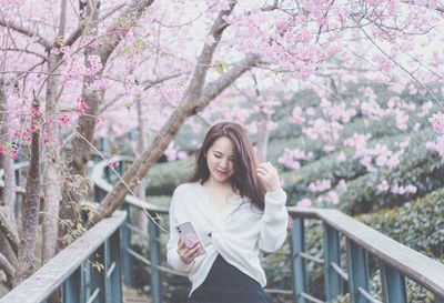 Young woman standing by cherry blossom tree