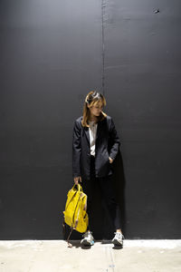 Businesswoman with backpack standing against wall at railroad station